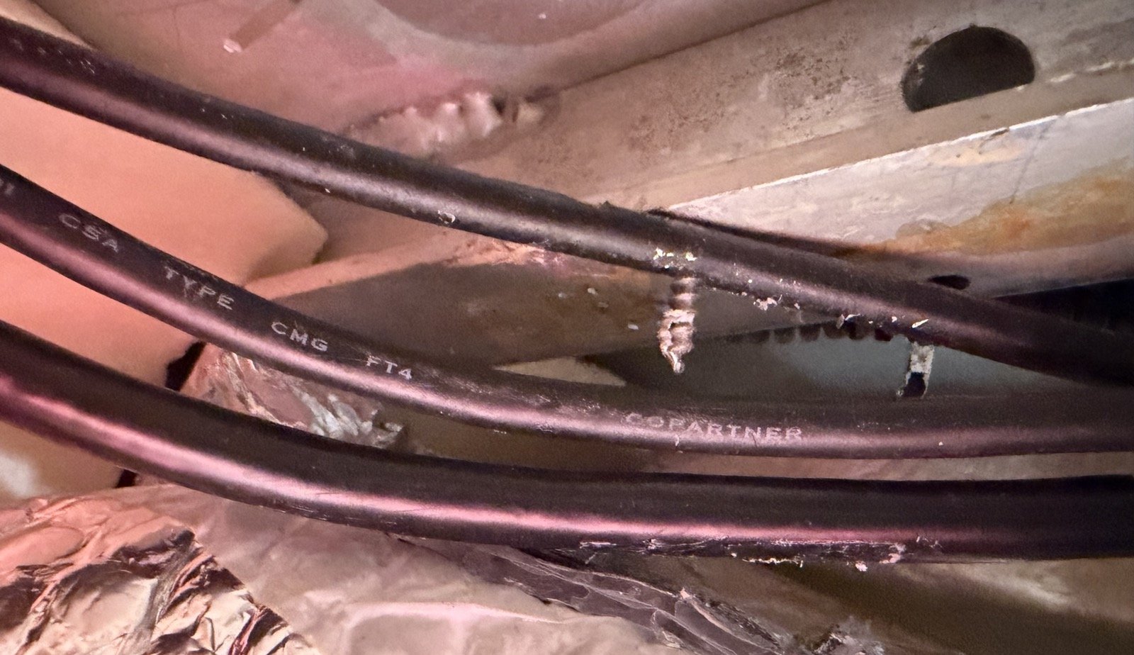 Behind the ceiling panel: a screw has pierced straight through a black cable running along the ceiling